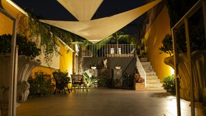 An outdoor patio area with a staircase leading to an upper level, surrounded by yellow walls and various plants.