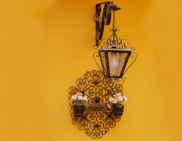 A wall-mounted metal lantern with a decorative metalwork design, two potted plants, and a hanging metal piece. - Cedofeita Village in Porto - Entire Condominium with Garden and Terraces (Porto)