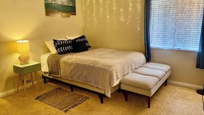 Une chambre à coucher avec un lit, une table de chevet, une lampe et une fenêtre avec des rideaux.