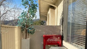 Un petit patio extérieur avec une pelouse artificielle, une table en verre, un réfrigérateur rouge de la marque Coca-Cola et un banc en pierre.