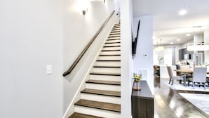 Un escalier avec des marches en bois et une rampe métallique, menant à un coin repas équipé d’une table et de chaises.