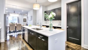 Une cuisine moderne dotée d’un grand îlot central, d’appareils électroménagers en acier inoxydable et de luminaires suspendus.