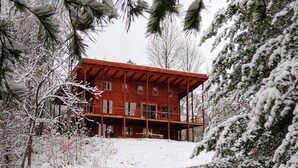Una cabaña de madera de dos pisos con balcón, rodeada de árboles cubiertos de nieve.
