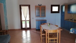 Ein Essbereich mit Tisch und Stühlen, eine Küche mit blauen Schränken und ein Fenster mit Vorhängen.