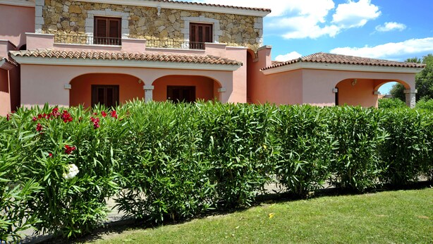 Ein zweistöckiges Haus mit Naturstein-Fassade, mehreren Balkonen und einem gepflegten Garten mit roten Blumen.
