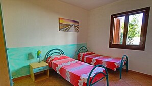 Ein Schlafzimmer mit zwei Einzelbetten, einem Nachttisch, einem Fenster mit Fensterläden und einem Bild an der Wand.
