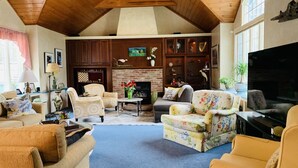 A spacious living room with high ceilings, wooden beams, a fireplace, and comfortable seating. - Lg Victorian, New Resort-likePrivate Pool, Beds for 17, 10min to SH beach (Cape May Court House)