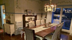 A dining room with a wooden table, white chairs, a chandelier, and a view through a glass door. - Lg Victorian, New Resort-likePrivate Pool, Beds for 17, 10min to SH beach (Cape May Court House)