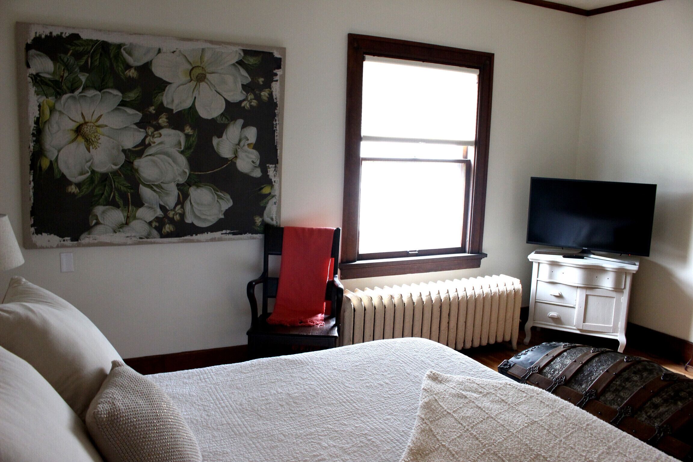 A bedroom with a bed, a chair, a television, a radiator, and a window.