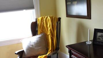 Ein Zimmer mit einem Holzschaukelstuhl, einem kleinen Tisch mit Kerze und einem gerahmten Bild an der Wand.