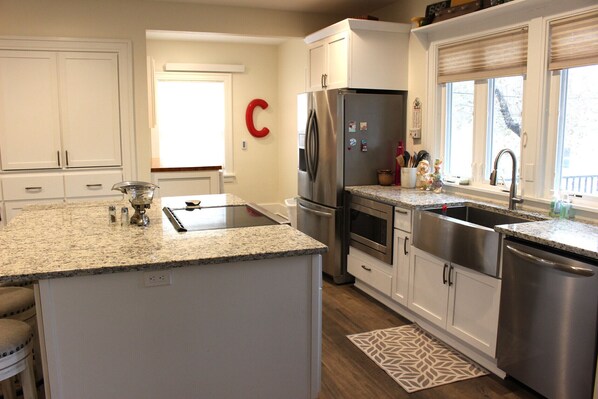 A modern kitchen with white cabinets, stainless steel appliances, a granite countertop, and a patterned rug.