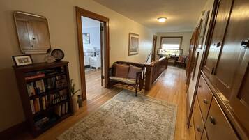 Un pasillo con suelo de madera, un tapete, una estantería y una puerta que da a otra habitación.