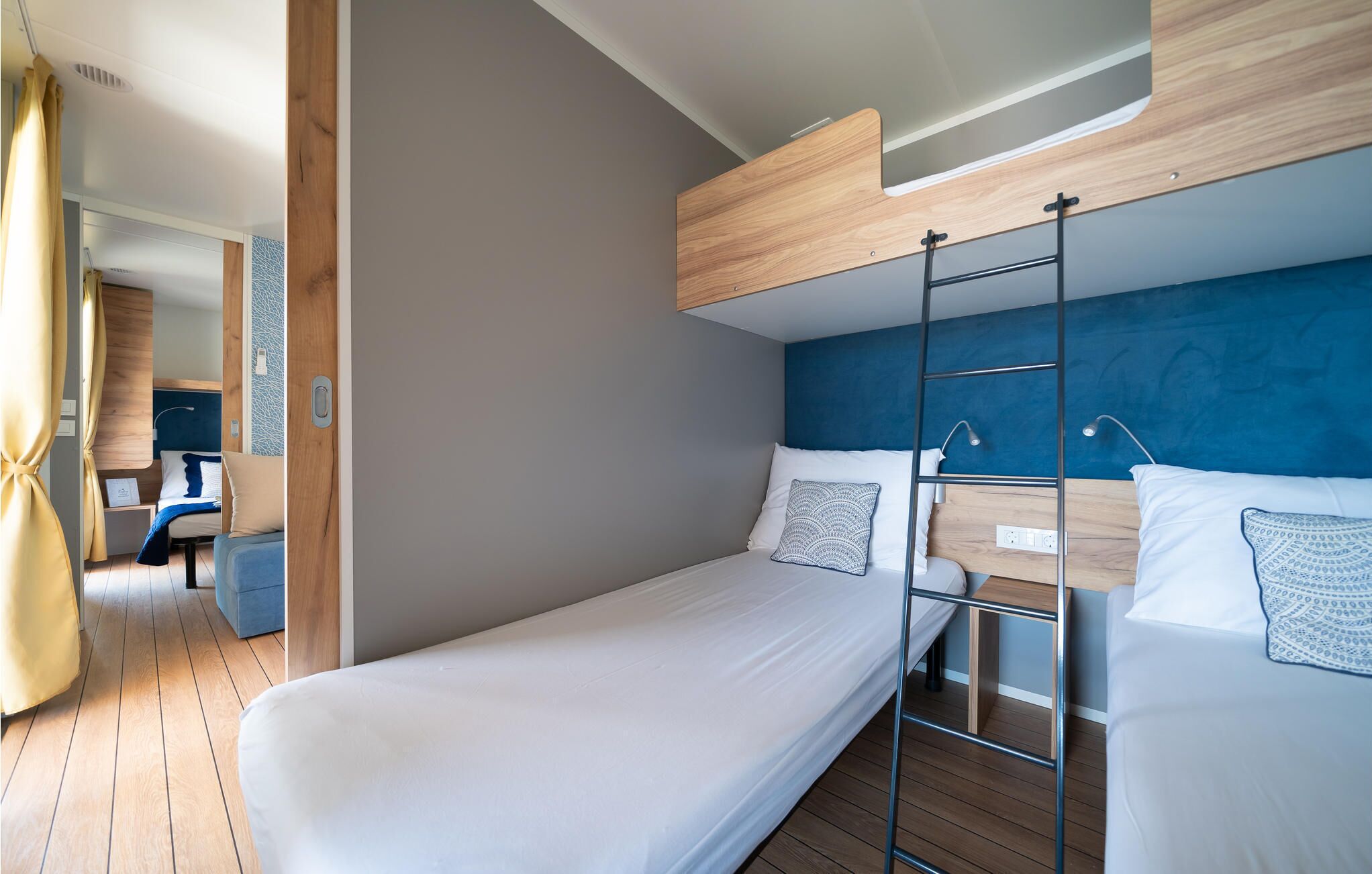 A modern, compact room with a bunk bed, a desk with a chair, and a small seating area.