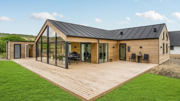 Een modern huis met een ruim terras, glazen deuren en een eethoek.