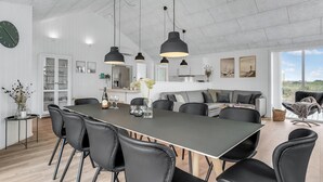 Een moderne keuken met een groot eiland, zwarte stoelen, hanglampen en uitzicht op de omgeving.