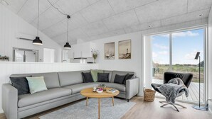 Een moderne woonkamer met een grijze bank, een ronde salontafel en uitzicht op het strand door grote ramen.