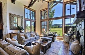 A spacious living room with large windows, a stone fireplace, and a cozy seating area. - Luxury Teton Springs Rental Home (Victor)