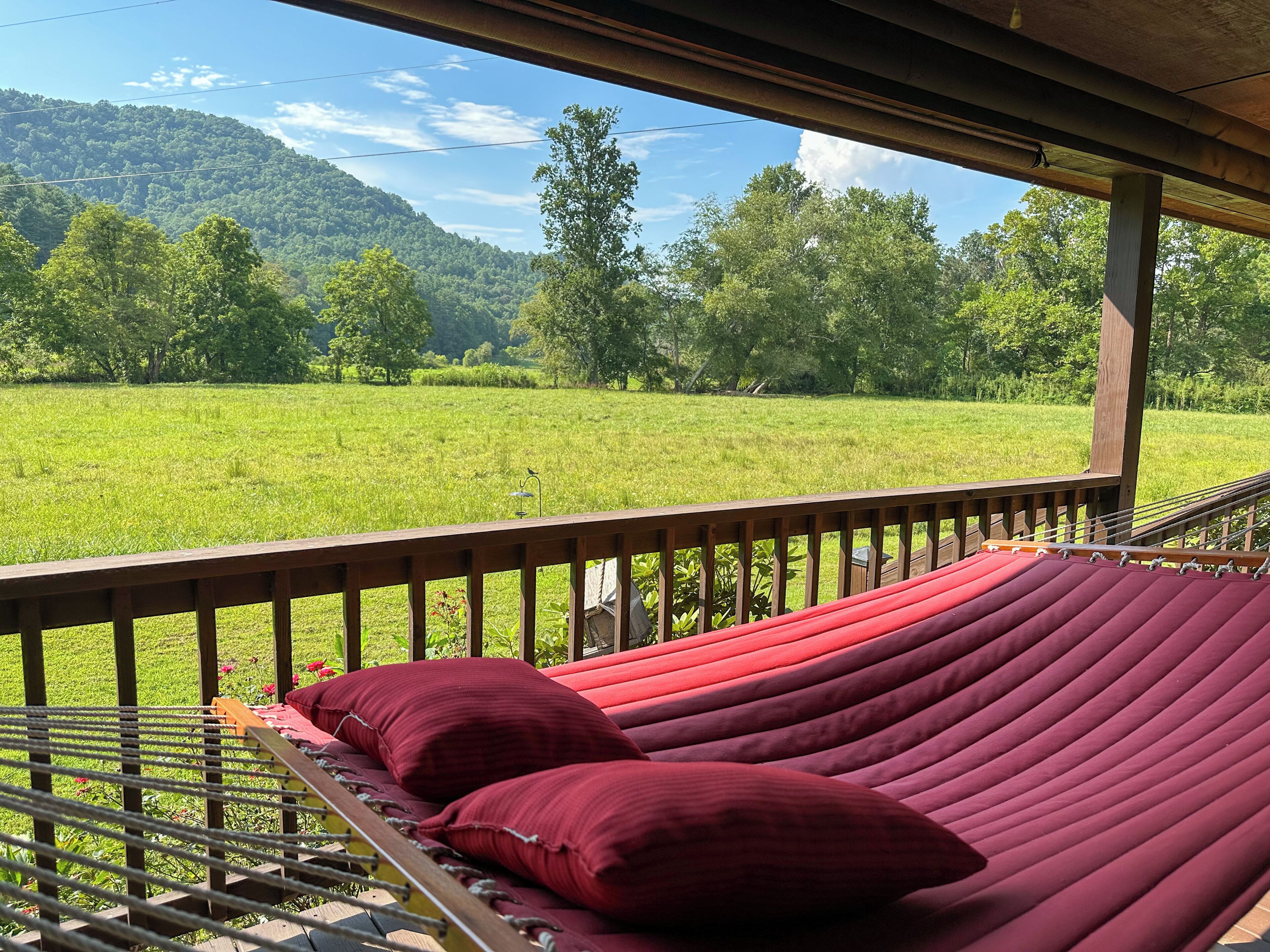 Una hamaca en una terraza de madera con vista a un campo verde y árboles.