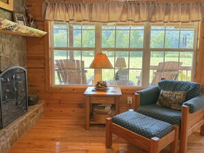 Ein gemütliches Zimmer mit einer hölzernen Bank, einem Tisch mit Lampe und Blick auf Gartenmöbel durch ein großes Fenster.