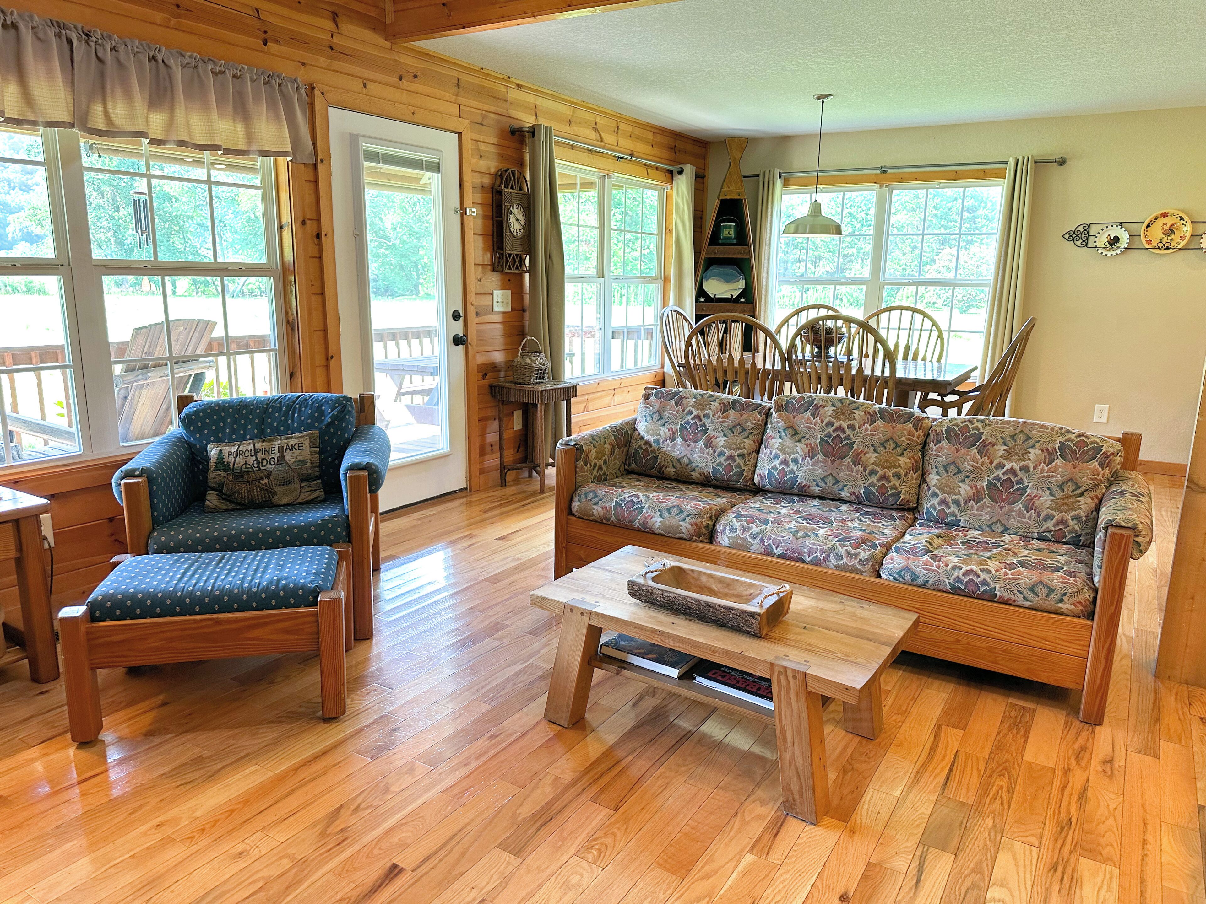 A wooden-floored living room with a blue armchair, a patterned sofa, and a wooden coffee table.