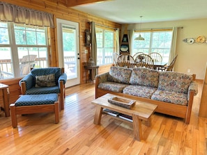 A wooden-floored living room with a blue armchair, a patterned sofa, and a wooden coffee table.