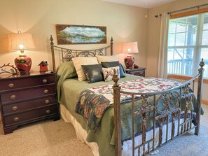 A bedroom with a bed, two nightstands, a lamp, a painting, and a window with blinds. - Riverfront cabin located in the N.E. Georgia Mountains minutes from Lake Chatuge (Hiawassee)