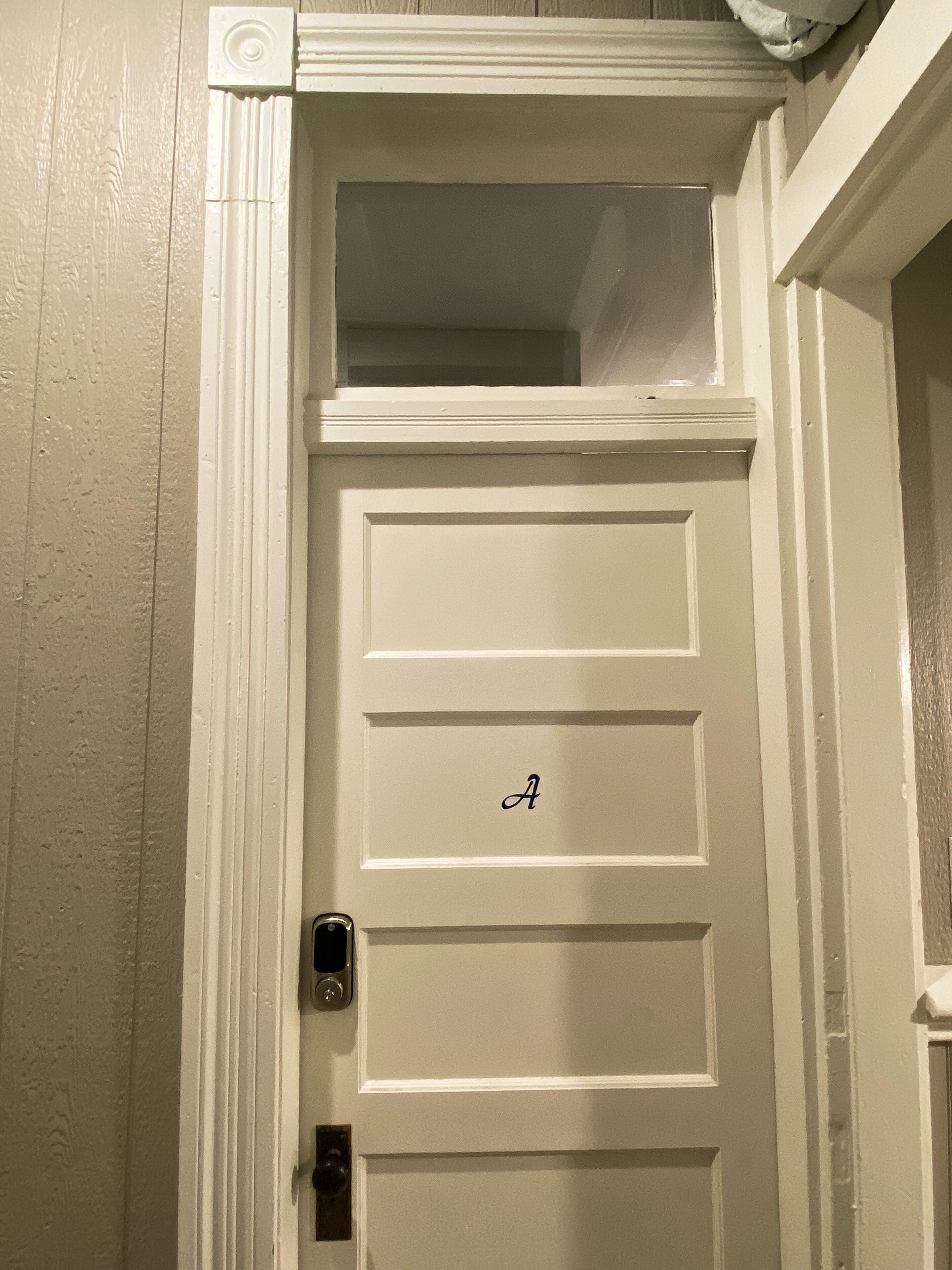 Uma porta branca com uma pequena janela no topo e a letra 'A' na porta.