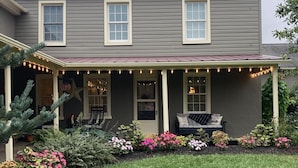 A two-story house with a covered porch, a small garden with various plants and flowers, and a neatly trimmed lawn.