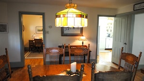 A dining room with a wooden table, six chairs, a hanging stained glass light fixture, a candle, and a framed picture on the wall.