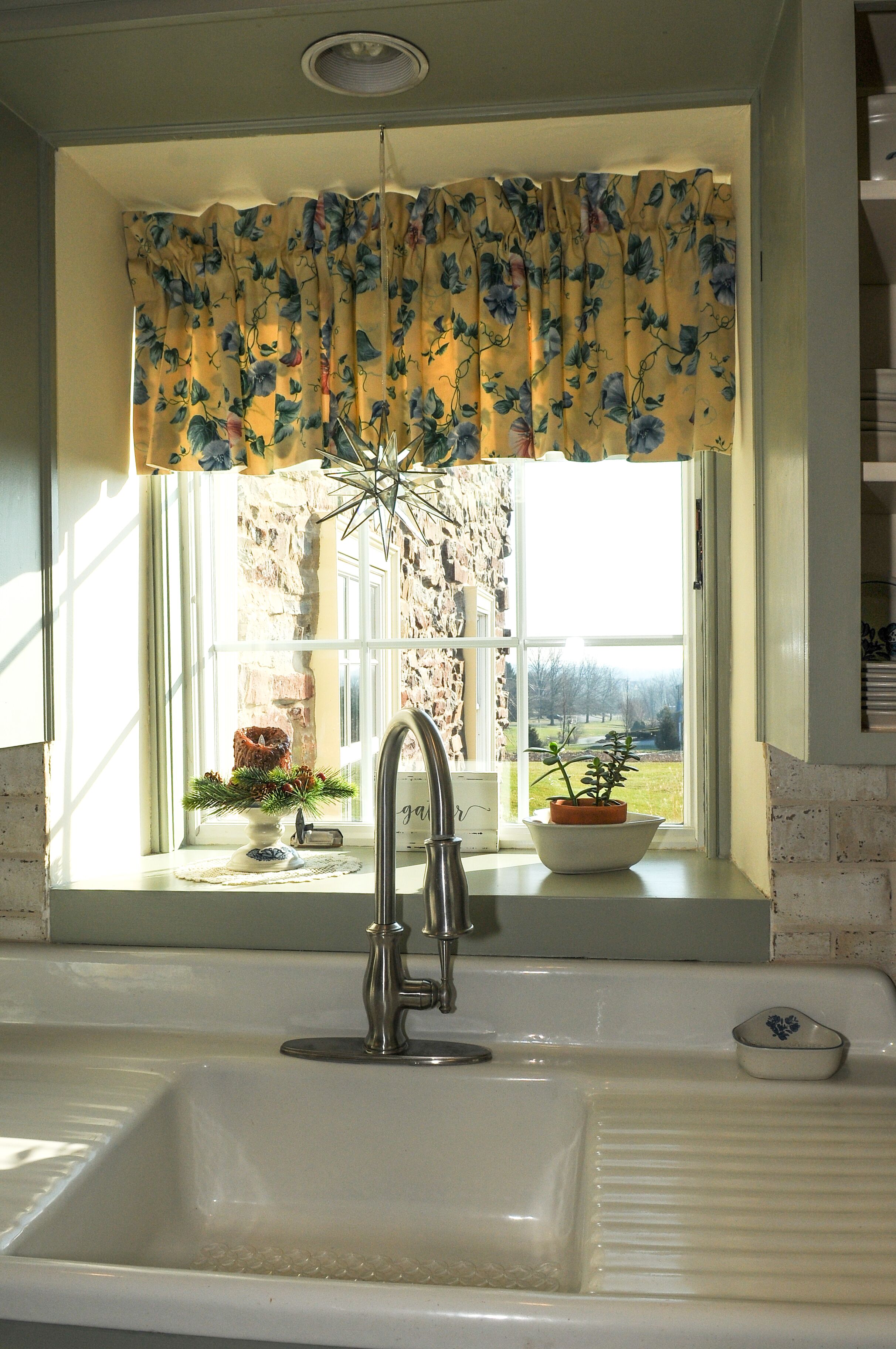 A kitchen sink with a window above it, a decorative star above the window, and a potted plant on the windowsill.