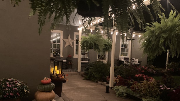 A garden pathway leading to a house with a star decoration, string lights, and various plants.