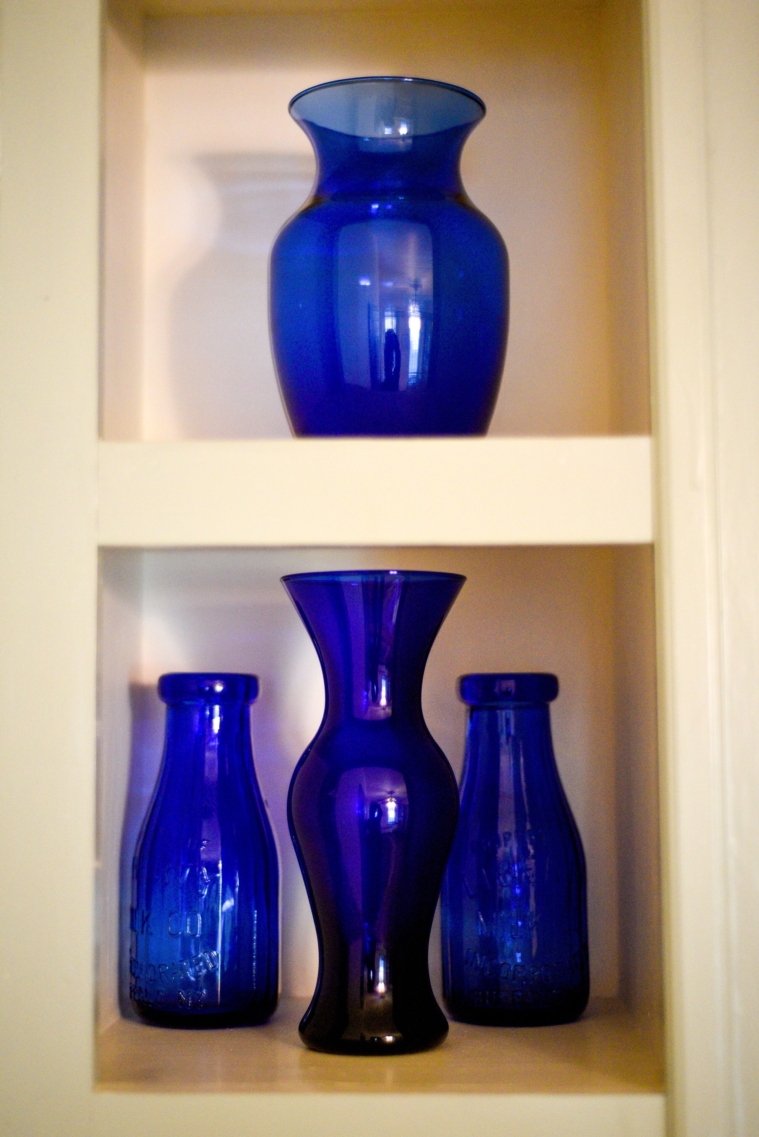 A shelf with three blue glass vases of varying shapes.