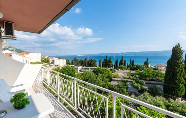 A balcony with a view of the sea, buildings, and greenery.