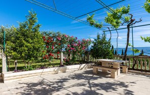 An outdoor seating area with a view of the sea, surrounded by trees and a pergola with climbing plants.