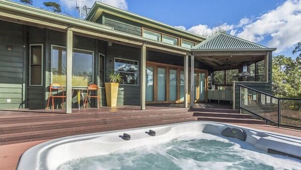 Una casa moderna con un jacuzzi, un patio cubierto y un comedor con mobiliario de exterior.