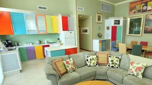Una sala moderna con un sofá seccional gris, armarios coloridos, un comedor y obras de arte en las paredes.