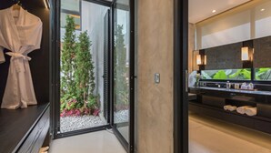 A modern bathroom with a glass door leading to a garden, a black vanity with a mirror, and a towel rack. - Villa NVL Canggu by Nagisa Bali (Canggu)