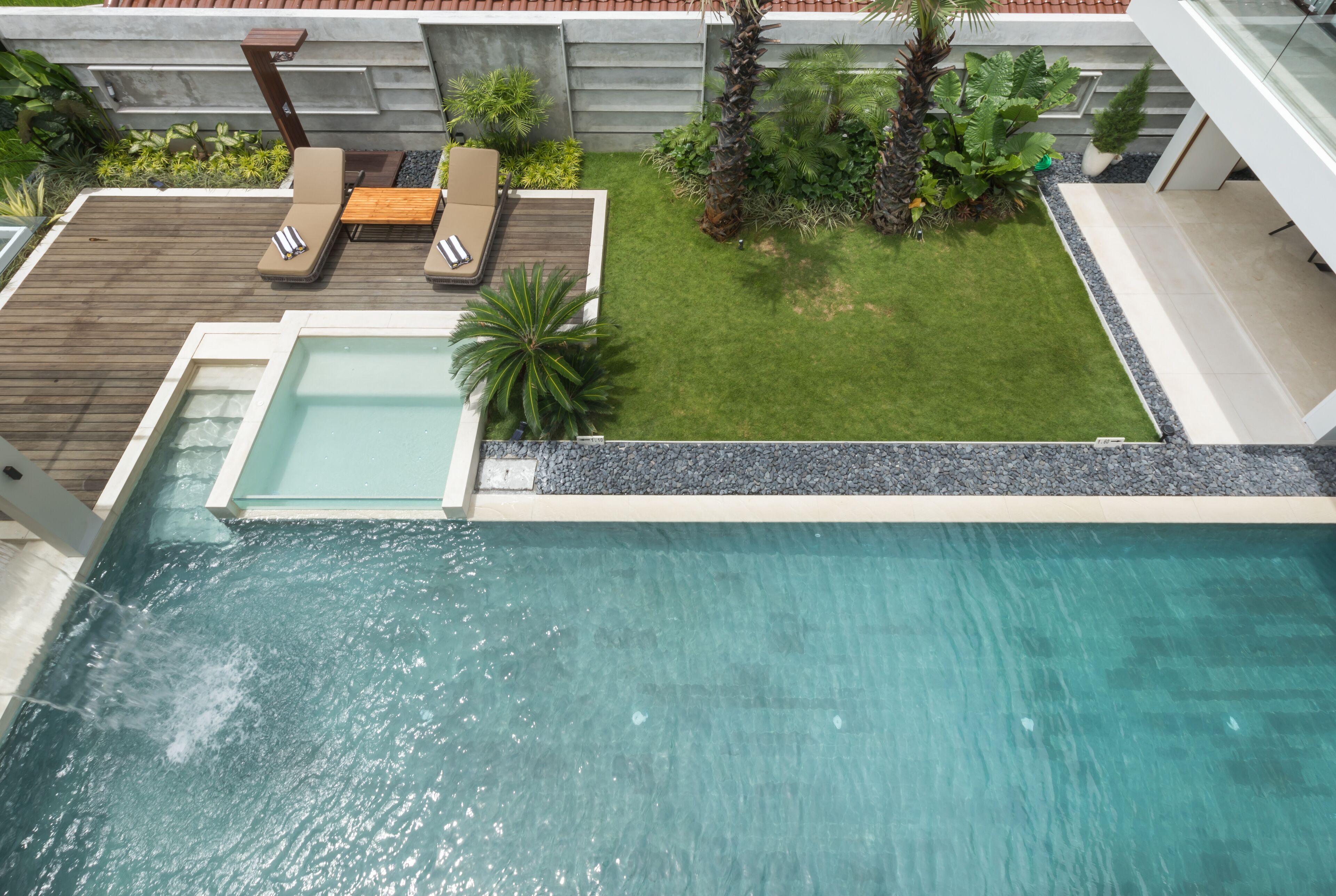 A modern outdoor pool area with a wooden deck, lounge chairs, and a small lawn.