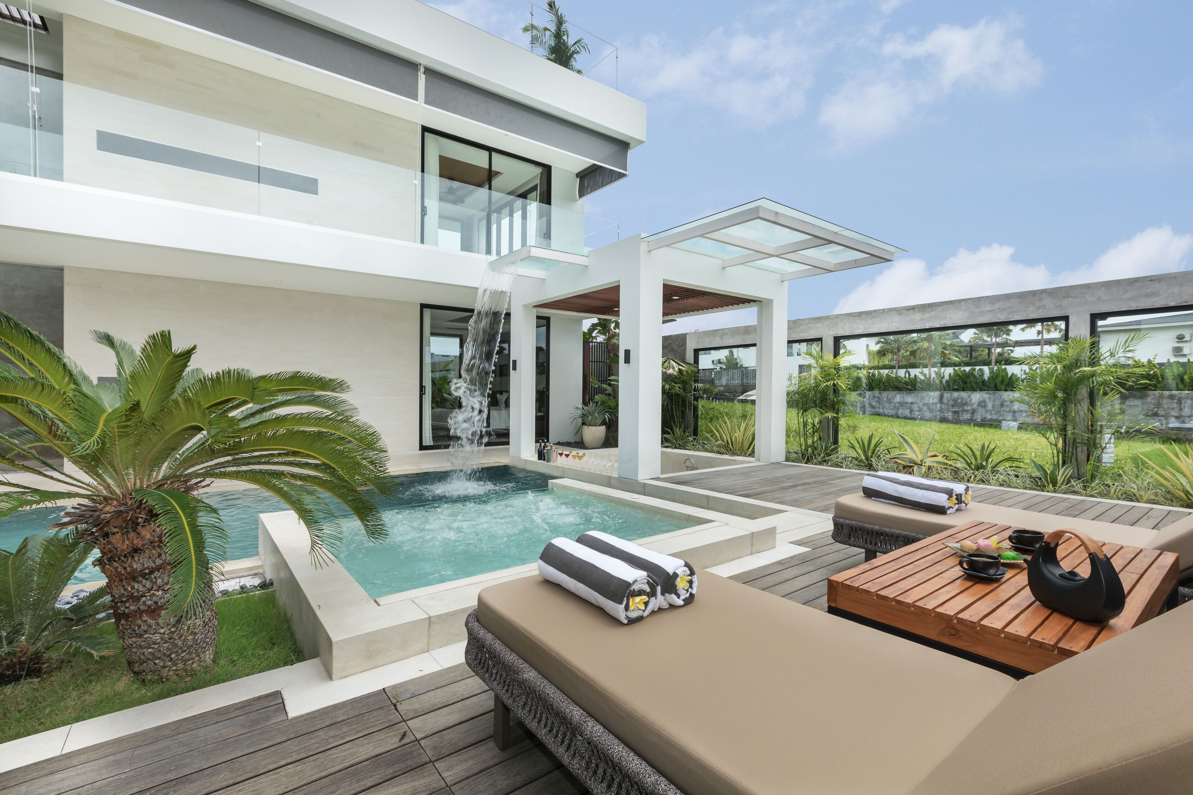 A modern outdoor pool area with a waterfall, lounge seating, and a wooden deck.
