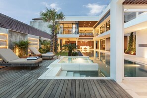 A modern outdoor pool area with lounge chairs, a hot tub, and a wooden deck. - Villa NVL Canggu by Nagisa Bali (Canggu)