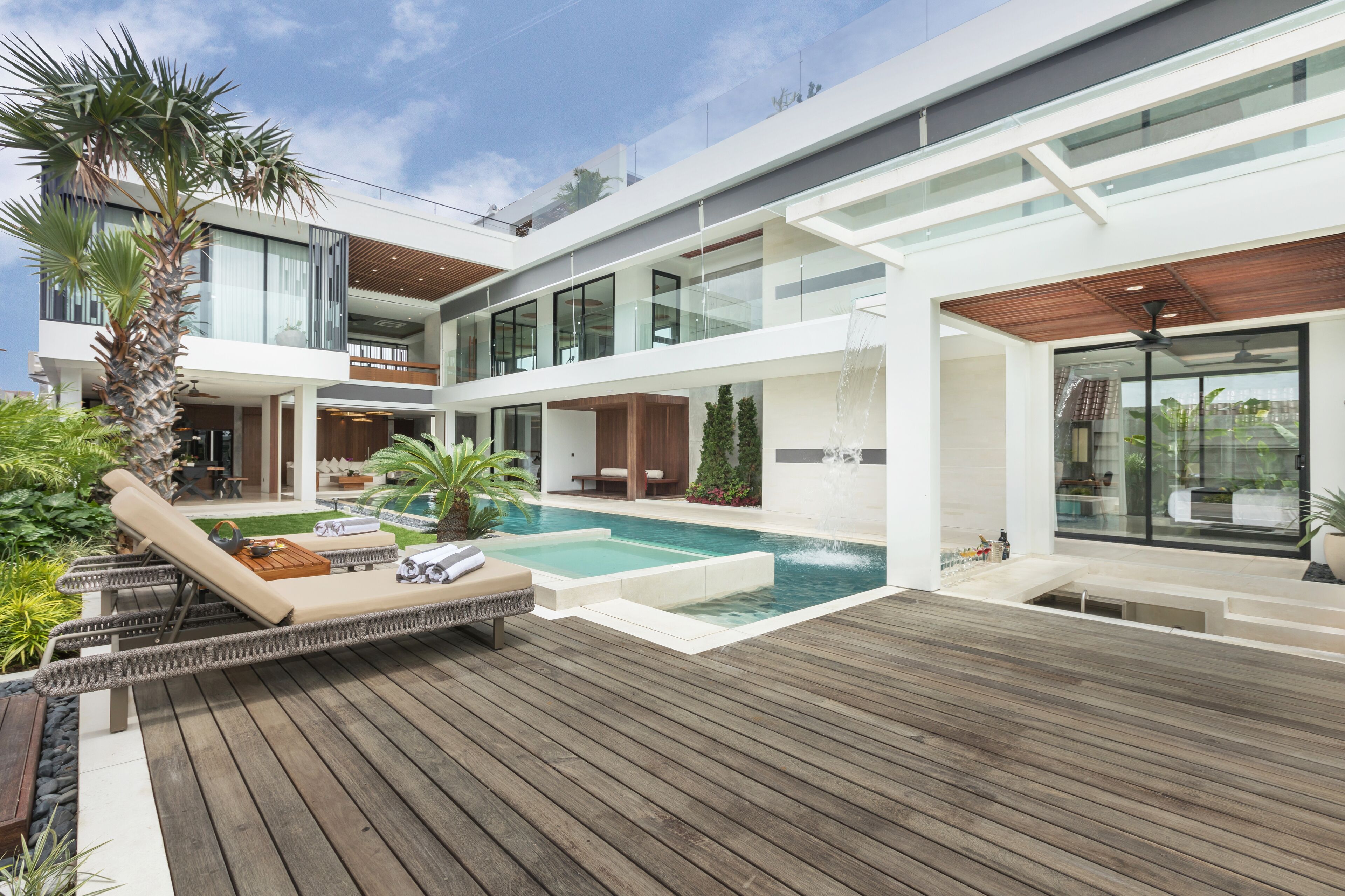 A modern multi-story house with a pool, wooden deck, and outdoor seating area.