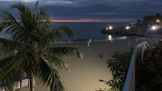 Een strand met palmbomen, een rotsformatie met verlichting, en een ondergaande zon.