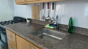 Een keuken met granieten werkbladen, houten kastjes en een roestvrijstalen spoelbak, met verschillende keukengerei erboven.