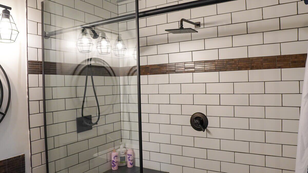 A glass-enclosed shower with a handheld showerhead, a wall-mounted towel rack, and a towel rack.