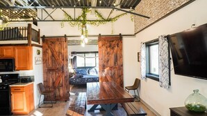 Un intérieur rustique avec une table à manger en bois, un coin cuisine et un téléviseur fixé au mur.