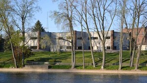 Vista al río de un edificio moderno con techo plano, rodeado de árboles y un área verde.