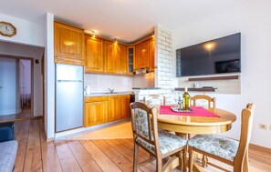 A compact kitchen with wooden cabinets, a built-in oven, and a dining area with a round table and chairs. - Stunning apartment in Duce with house sea view (Duce)