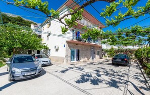 A residential street with parked cars, a white building with a red roof, and a balcony with clothes hanging. - Stunning apartment in Duce with house sea view (Duce)