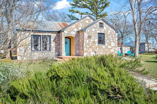 Une maison en pierre avec une porte bleue, entourée de verdure et d’arbres.