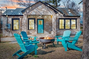 Une maison en pierre avec un foyer extérieur et des fauteuils Adirondack turquoise dans la cour.